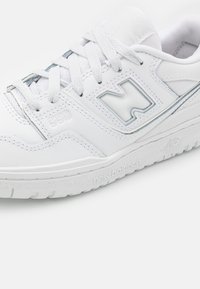 Baskets blanches New Balance 550 avec lacets blancs et logo, coutures détaillées et logo en relief sur la semelle et le panneau latéral.