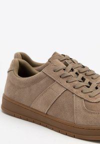 Braune Wildleder-Sneaker mit strukturierter Oberfläche, runder Zehenpartie, flachen Schnürsenkeln und einer Gummisohle mit leichtem Profil.