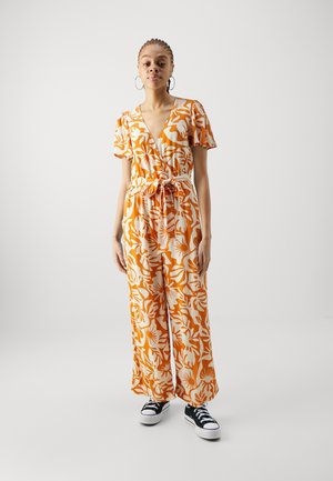 Orange and white floral jumpsuit with a v-neck, short sleeves, cinched waist, wide legs, and worn with black sneakers.