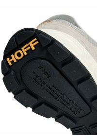 Zwarte rubberen buitenzool met het geperste merknaam "HOFF." Bovenkant van beige suède en grijze accenten, met een gestructureerd ontwerp voor grip.