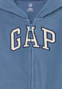 Blå fleece baby hettejakke med frontglidelås, store "GAP" bokstaver på brystet, størrelse 0-3 måneder, laget i Kambodsja.