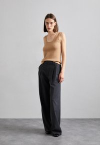 Débardeur ajusté en matériau doux ; associé à un pantalon ample gris foncé avec des plis, porté avec des chaussures noires.
