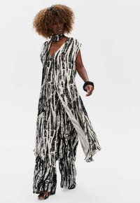Zwart-wit gestreepte jumpsuit met een diepe V-hals, kapmouwen en zijsplitten. Zachte stof met een vloeiende vormgeving en een bijpassende nek-sjaal.