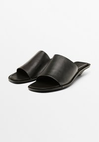 Zwarte leren instappersandalen met een open teen en een lage hak, met een soepele textuur en een minimalistisch ontwerp.