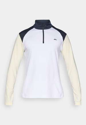 Hosszú ujjú fehér és krém színű sportfelső fekete vállpanelekből, félig cipzáros előlappal, és kis fekete logóval a mellrészen.