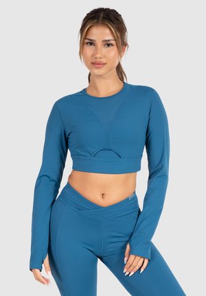 Langsleeve crop top in teal, met een ronde halslijn en een gebogen uitsnijding. Zachte, rekbare stof met een getailleerde pasvorm.