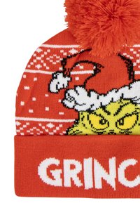Rode gebreide beanie met een groene Grinch-afbeelding, witte tekst met "GRINC" en een pluizige oranje pompon bovenop.