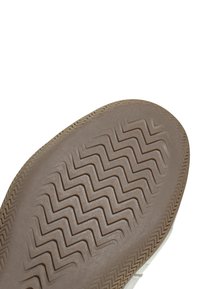 Suola di sneaker in gomma beige con motivo a zigzag. Bordo liscio e arrotondato con finitura lucida discreta. Area della punta rinforzata visibile.