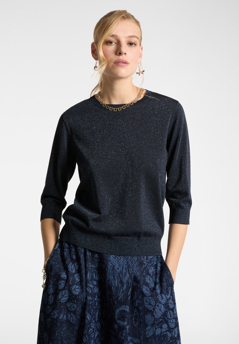 Maglione in tessuto lavorato blu navy, scintillante, con maniche a tre quarti e scollatura rotonda; abbinato a una gonna blu con motivo floreale a trama.