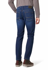 Dunkelblaue Jeans mit schmaler Passform, ausgestattet mit zwei Gesäßtaschen und detaillierten Nähten. Kombiniert mit braunen High-Top-Sneakern.