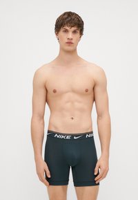 Vīriešu Nike bokseršortos tumši zaļā krāsā ar melnu logotipa jostasvietu. Audums izskatās gluds, pieguļošs un paredzēts komfortam.
