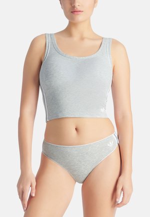 Frau trägt ein graues ärmelloses Crop-Top und passende Bikini-Unterwäsche mit weißem Adidas-Logo und Streifen vor weißem Hintergrund.