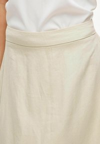 Jupe beige avec une texture lisse et légère, dotée d'une taille ajustée et d'un design en A qui s'évase vers le bas.