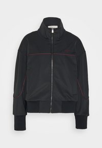 Giacca nera con zip, realizzata in un tessuto liscio, con colletto alto, polsini a costine e cuciture di accento rosse sulle spalle e sul petto.