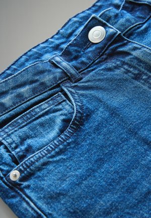 Modré džíny z denimu s klasickým designem, přední kapsou a bílým knoflíkem na pase, které mají mírně vybledlou texturu.