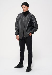 Czarna skórzana kurtka bomberka z wysokim kołnierzem, zamkiem z przodu, ściągaczami na mankietach i boczną kieszenią. W zestawie z czarnymi spodniami i trampkami.