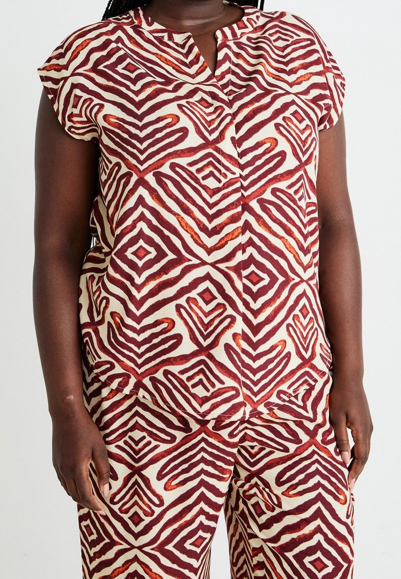 Femme portant un haut à manches courtes et un pantalon assorti avec un motif géométrique losange rouge et beige.