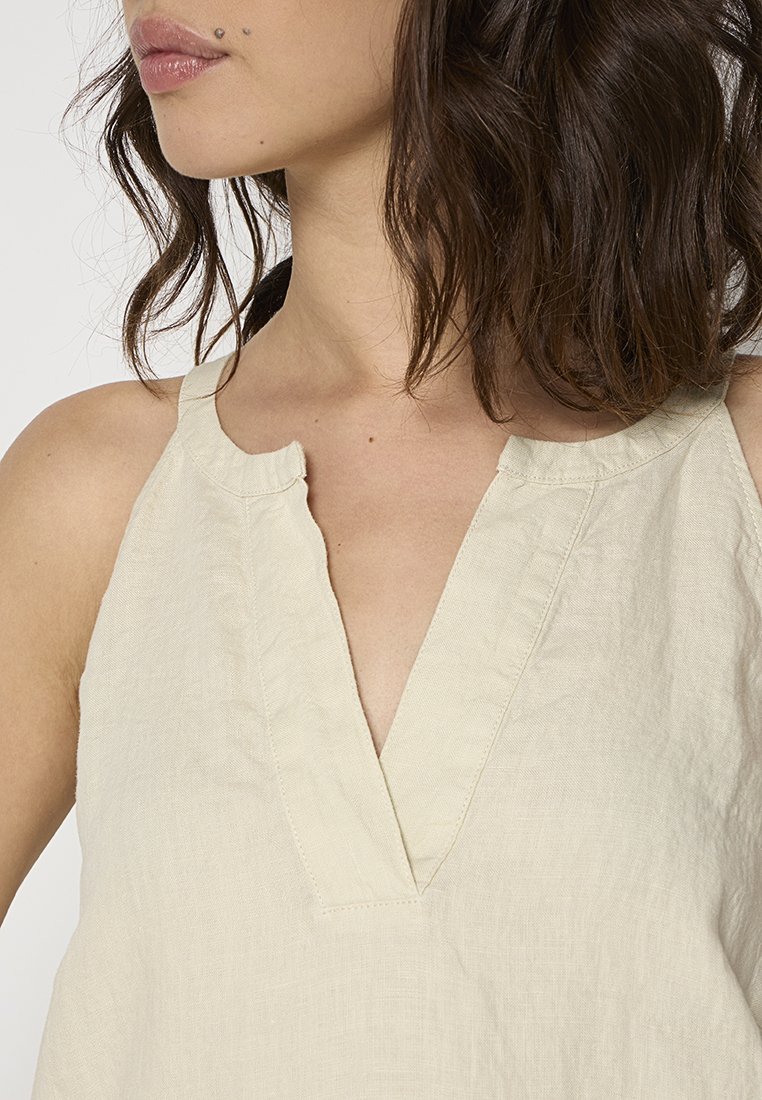 Helles beiges Leinenoberteil mit V-Ausschnitt und ärmellosem Design, das eine leicht strukturierte Oberfläche und saubere Nähte aufweist.