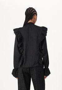 Blusa negra con acentos de encaje con volantes, cuello alto y mangas largas. Presenta puños texturizados y un acabado de tela suave.