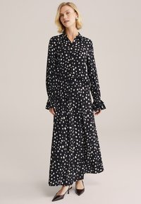 Melnas blūzes un svārku komplekts ar baltām punktiņām. Garas piedurknes ar uzplaiksnītiem aprocēm, plūstoša silueta, un tumšas kurpes ar smailiem purngaliem.