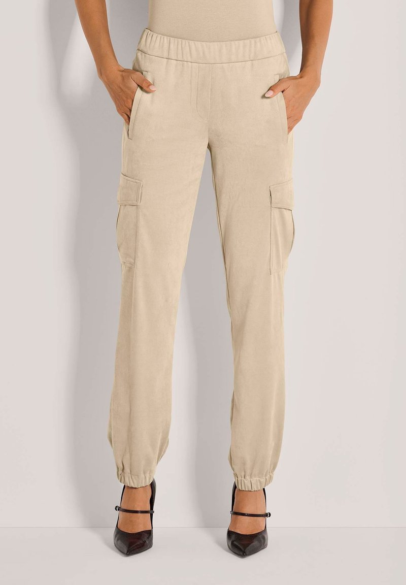 Beige cargobroek met een elastische tailleband, twee zijzakken en twee zijcargozakken. Tapered boorden bij de enkels. Gladde textuur.