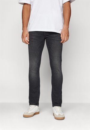 Dark gray slim-fit jeans made of denim, featuring a clean design and subtle fading. Worn with white sneakers and a loose white t-shirt.