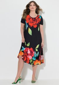 Czarna sukienka w kwiaty z jaskrawymi czerwonymi różami i zielonymi liśćmi. Krótkie rękawy, długość do kolan, lejący fason. Noszona z zielonymi szpilkami i małą czerwoną torebką.