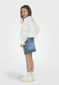 Bela bluzica z dolgimi rokavi z čipkastim robom, v kombinaciji z jeans krilom in belimi športnimi copati. Obleka je sproščena in primerna za otroke.