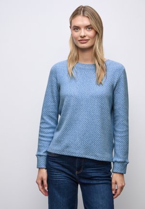 Jasnoniebieski sweter z długim rękawem, z diagonalnym wzorem teksturowanym i okrągłym dekoltem, zestawiony z ciemnoniebieskimi dżinsami. Miękki, luźny krój.