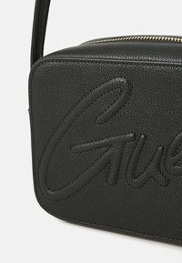Schwarze Leder-Crossbody-Tasche mit geprägtem Logo, glatter Textur, rechteckiger Form und goldenen Reißverschlussdetails.