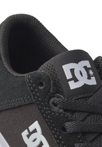 Adidași negri cu un exterior texturat, guler căptușit și un patch alb contrastant cu logo-ul. Șireturile și cusăturile sunt de asemenea negre.