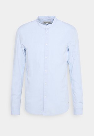 Sinih pitkähihaine paita, jossa on kaulakotelo, nappikiinnitys ja sileä puuvillan rakenne; sisältää valkoiset napit ja kaarevan helman.