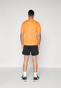 Orange athletic t-shirt, short sleeves, paired with black mesh shorts featuring white trim, worn with black shoes and white socks.