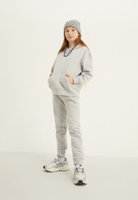 Pelēks flīsa kapuce ar priekšējo kabatu, apvienota ar atbilstošām biksēm. Pabeigta ar ribotu pelēku beanie un sudraba kedām.