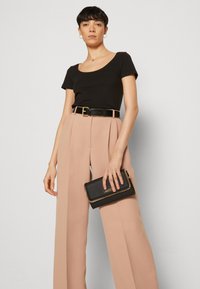 Camiseta negra ajustada combinada con pantalones beige de pierna ancha de talle alto y un clutch negro con acentos de hardware dorado.
