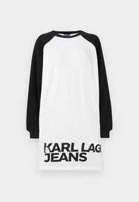 Vestido oversized em branco e preto com mangas raglan, apresentando texto em negrito preto "KARL LAGERFELD JEANS" na parte inferior. Material de algodão suave.