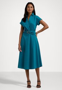 Vestido envolvente azul-água com mangas curtas, cintura cingida e saia rodada. Textura suave e detalhe de gola visível, combinado com sandálias pretas.