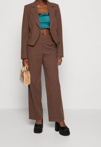 Blazer marrón ajustado, top corto verde azulado, pantalones de pierna ancha marrones, tacones de plataforma negros y un pequeño bolso beige. Texturas suaves y l�íneas limpias.
