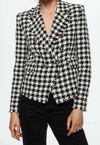 Doppelreihiger Blazer im schwarz-weißen Hahnentritt-Muster. Verfügt über goldene Knöpfe und eine strukturierte Stoffoberfläche. Taillierter Schnitt.