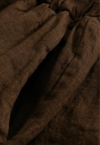 Tissu en lin brun foncé texturé avec plis de taille élastique froncée et une ouverture de poche sur un vêtement.