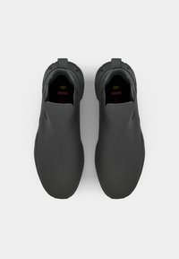 Top view of two sleek, modern black slip-on shoes with a minimalist design and textured soles against a plain white background.