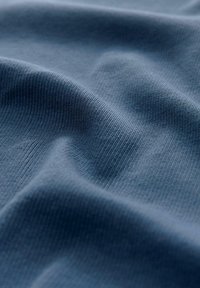 Sininen kohokuosiset kangas, jolla on sileä pinta, esittelee pehmeitä poimuja ja hienovaraisen kiillon, korostaen sen venyvyyttä ja kevyttä laatua.
