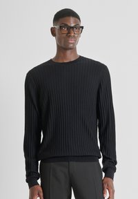 Maglione nero a costine con maniche lunghe e scollatura rotonda. Tessuto morbido, design aderente e leggera elasticità. Abbinato a pantaloni scuri.