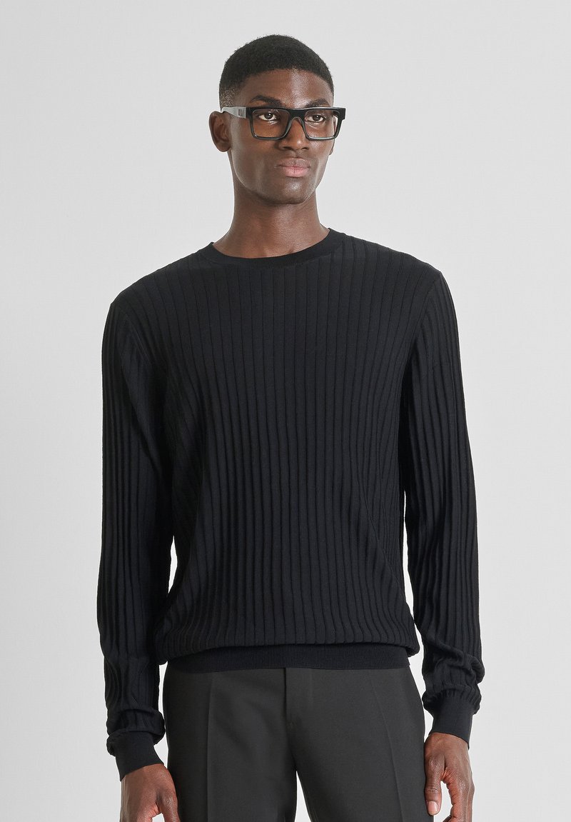 Maglione nero a costine con maniche lunghe e scollatura rotonda. Tessuto morbido, design aderente e leggera elasticità. Abbinato a pantaloni scuri.