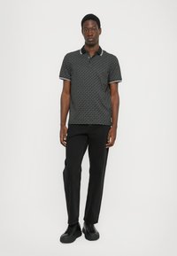 Polo noir avec un motif géométrique subtil, manches courtes et col contrasté ; associé à un pantalon noir et des chaussures noires.
