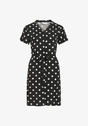 Musta lyhythihainen nappipaita-mekko, jossa on valkoisia pilkkuja ja samaa kangasta oleva vyö solmittuna vyötärölle.