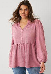 Pink textured blouse with a V-neck, button detail, and gathered waist. Features long, puffed sleeves and a relaxed fit.