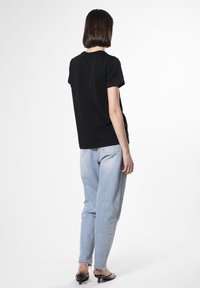Camiseta de algodón negra de manga corta, combinada con jeans de tiro alto en azul claro con dobladillos deshilachados y sandalias de tacón negras.