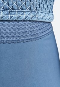 Abbigliamento attivo blu con un tessuto texturizzato a motivo diamante sulla parte superiore e uno strato inferiore liscio, entrambi in diverse tonalità di blu.