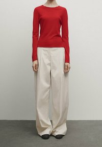 Haut rouge à manches longues associé à un pantalon large taille haute couleur crème. Le haut présente un col rond, tandis que le pantalon arbore une coupe ample et fluide.